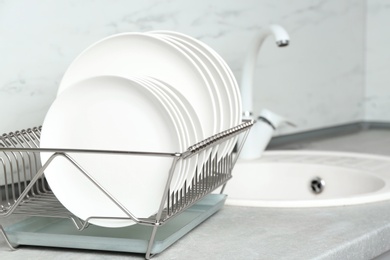Photo of Different clean plates in dish drying rack on kitchen counter
