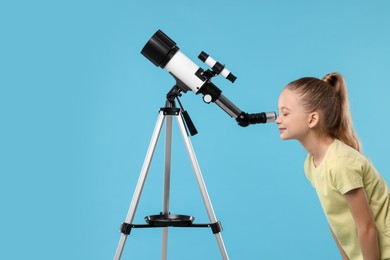 Happy girl looking at stars through telescope on light blue background, space for text