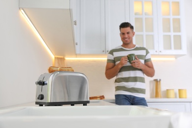 Photo of Man preparing breakfast in kitchen, focus on toaster with slices of bread