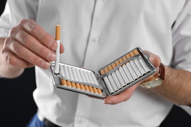 Photo of Man taking cigarette from holder on black background, closeup