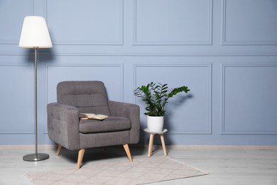 Photo of Cosy armchair, floor lamp and potted plant near light grey wall in room, space for text. Interior design