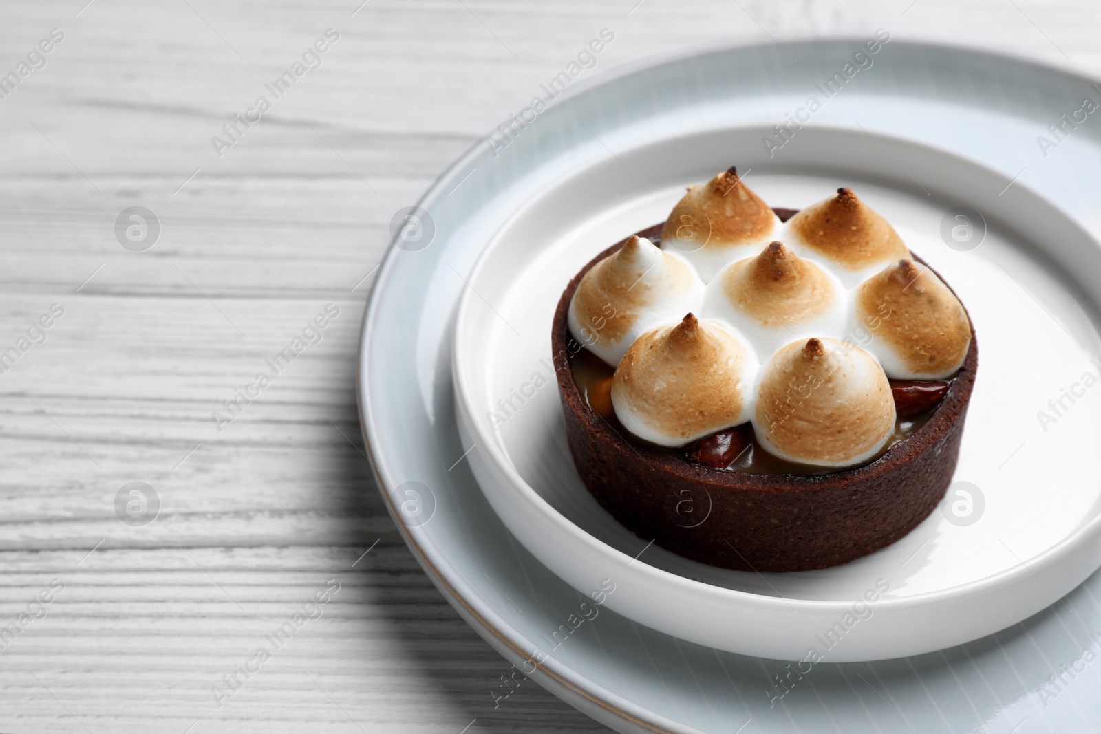 Photo of Delicious salted caramel chocolate tart with meringue on white wooden table, closeup. Space for text