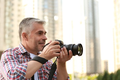 Photo of Handsome mature man taking photo with professional camera outdoors. Space for text