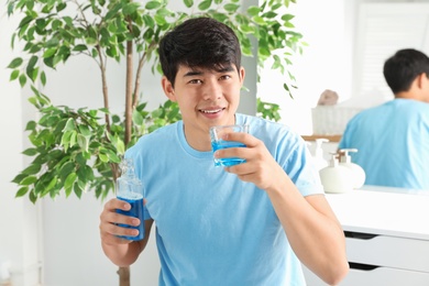 Man holding bottle and glass with mouthwash in bathroom. Teeth care