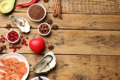 Photo of Natural aphrodisiac. Different food products and heart model on wooden table, flat lay. Space for text