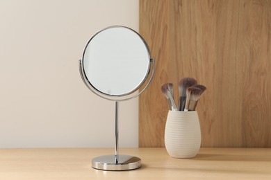 Mirror and makeup brushes on wooden dressing table in room