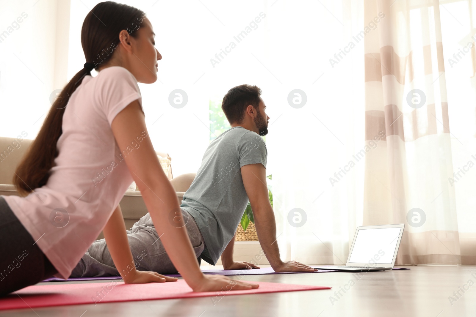 Photo of Couple practicing yoga while watching online class at home during coronavirus pandemic. Social distancing