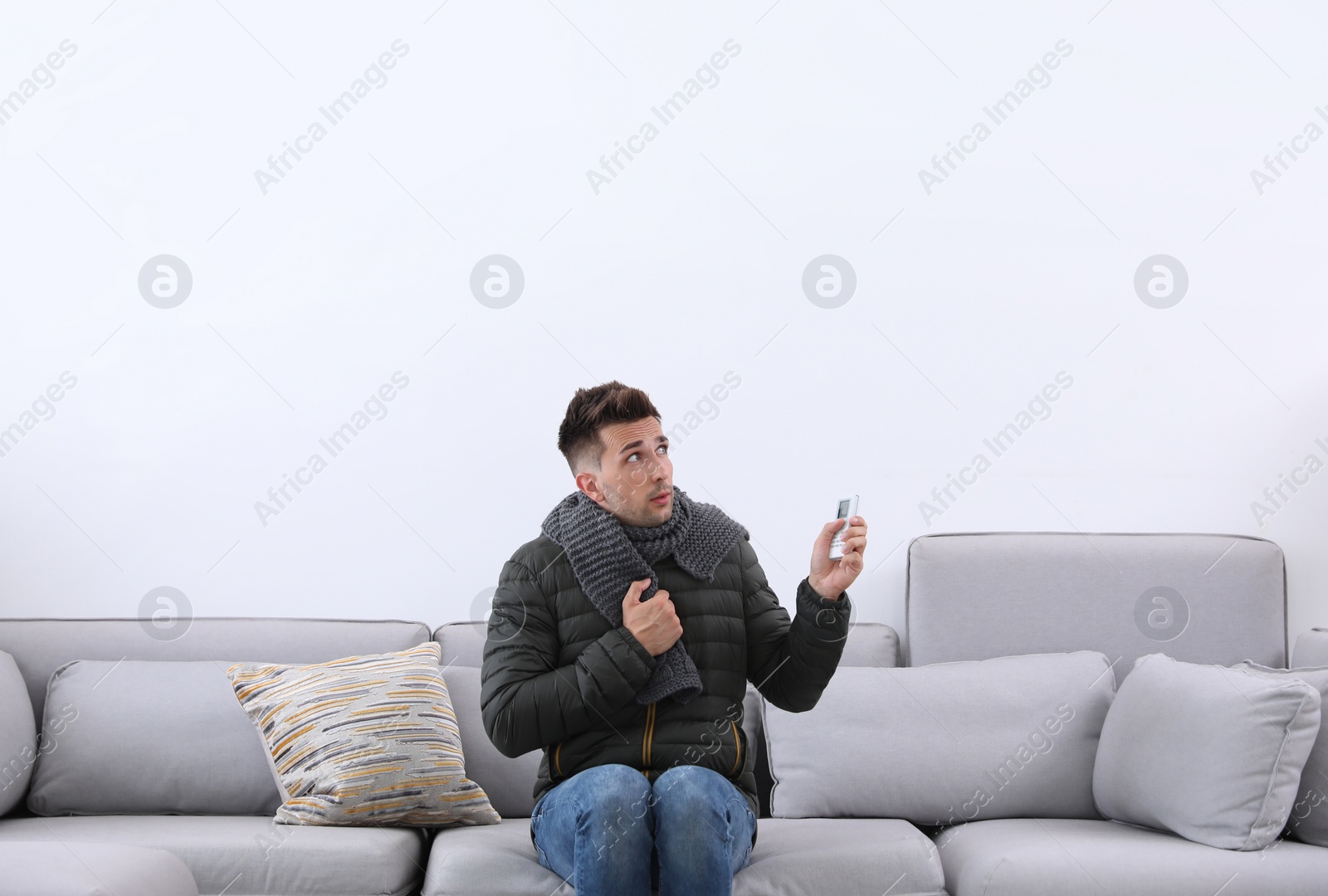 Photo of Young man with air conditioner remote control freezing on sofa at home