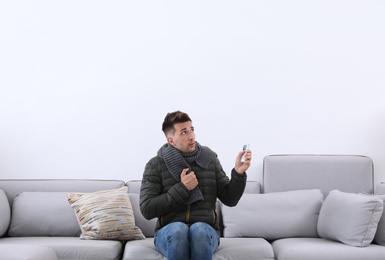 Photo of Young man with air conditioner remote control freezing on sofa at home
