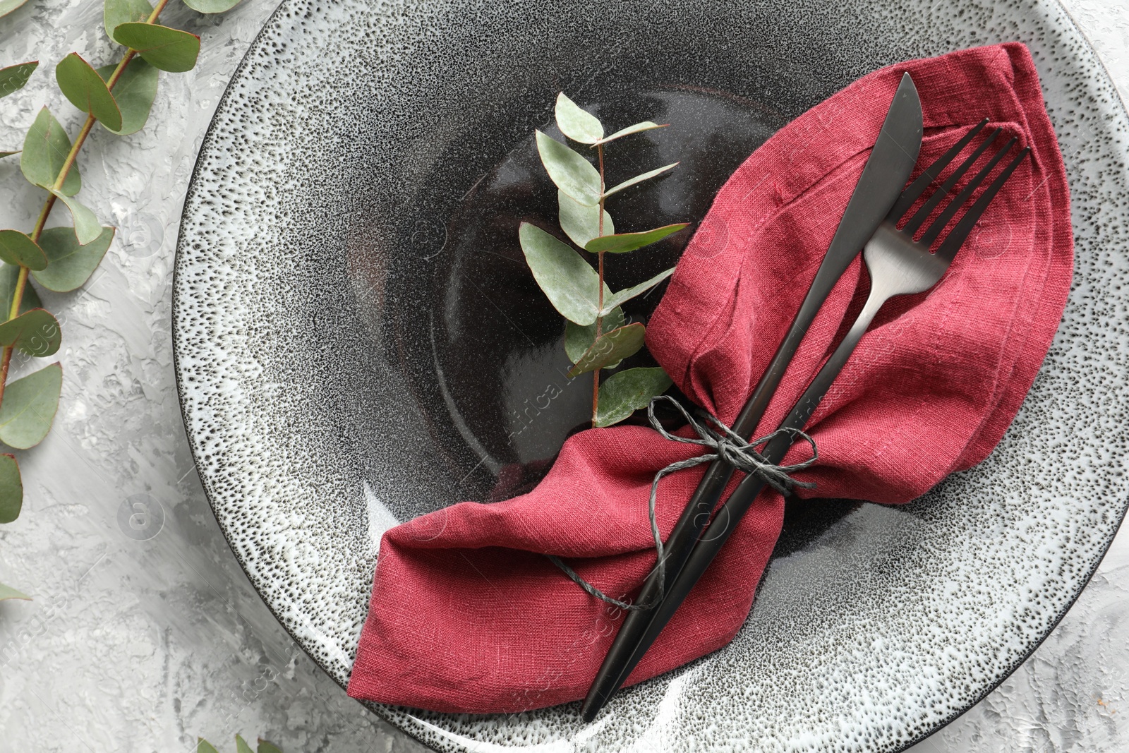 Photo of Stylish setting with cutlery, napkin, eucalyptus branches and plate on grey textured table, top view