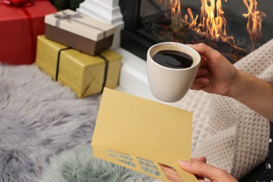 Photo of Young woman with greeting card and hot drink sitting indoors, closeup. Space for text