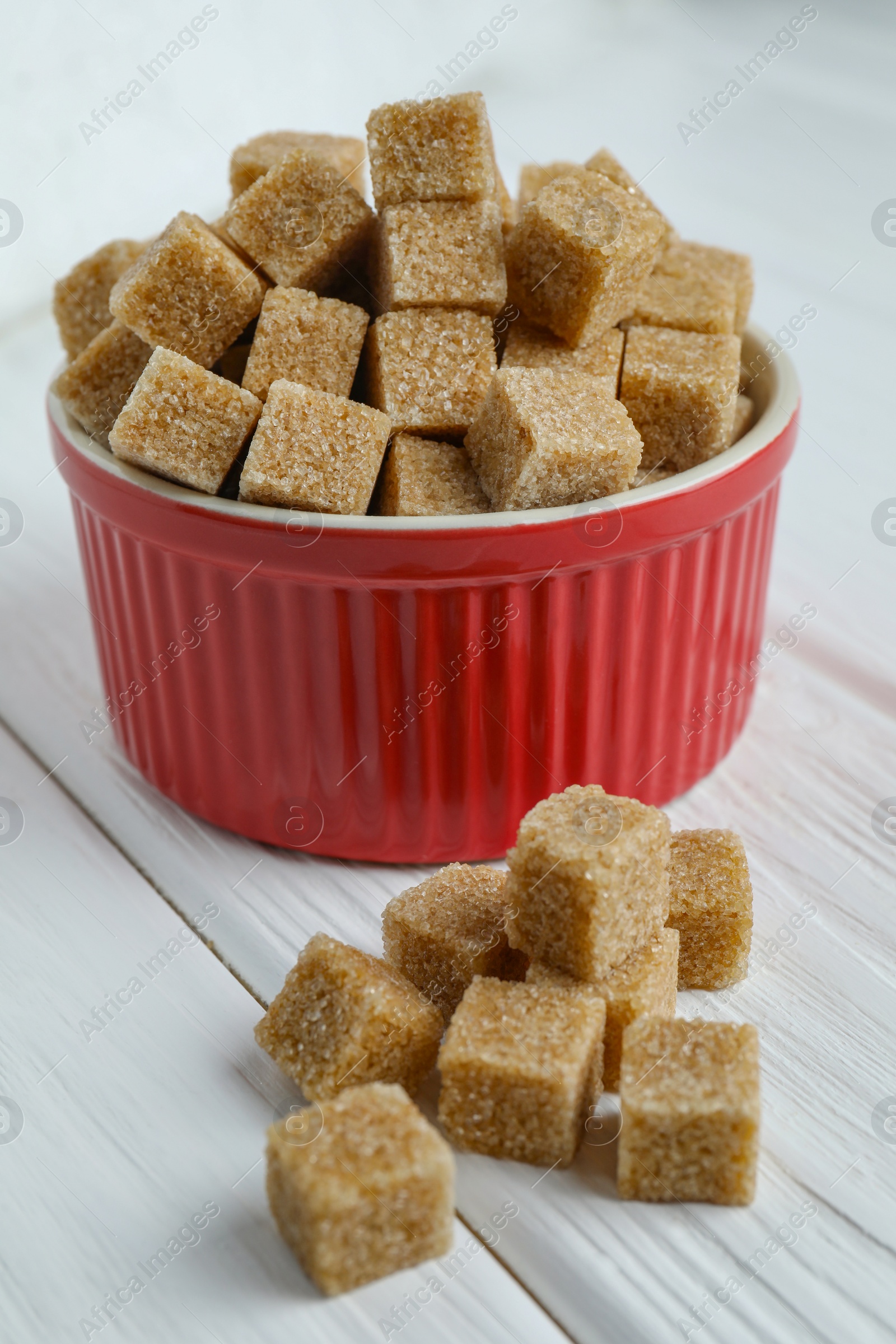 Photo of Brown sugar cubes in bowl on white wooden table, closeup