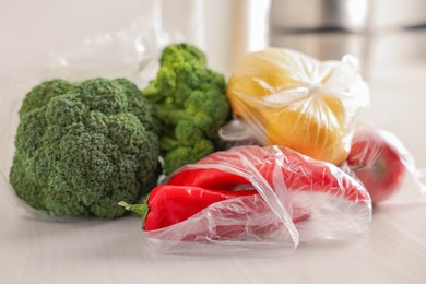 Plastic bags and fresh products on white table, closeup