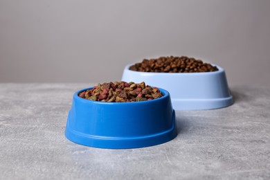Photo of Dry food in pet bowls on grey surface