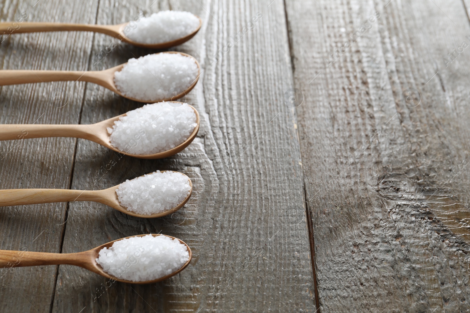 Photo of Organic salt in spoons on wooden table, space for text