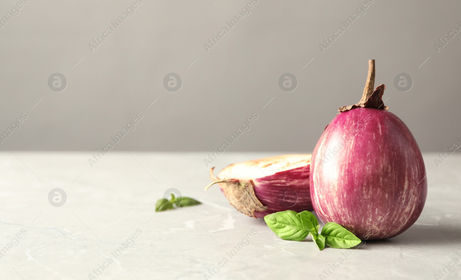 Photo of Ripe eggplants and basil on light grey marble table. Space for text