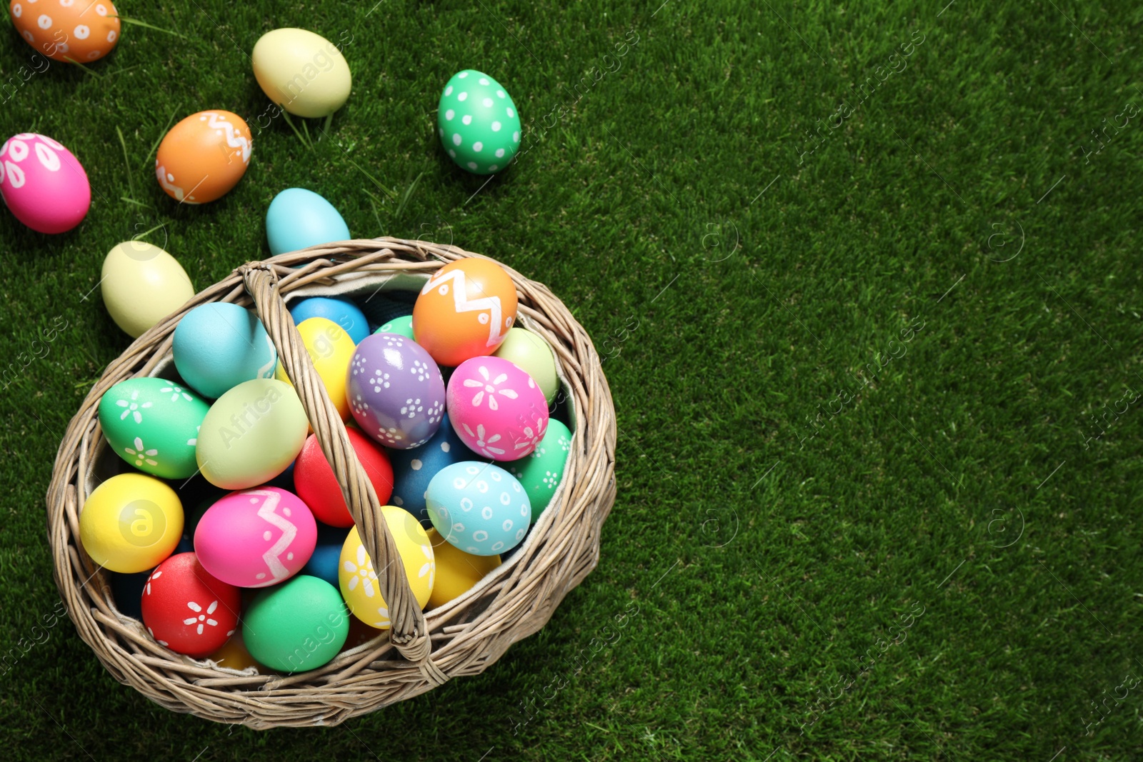 Photo of Colorful Easter eggs in basket on green grass, above view. Space for text