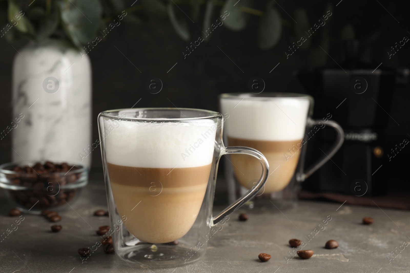 Photo of Glass cups of delicious latte macchiato and scattered coffee beans on grey table. Space for text