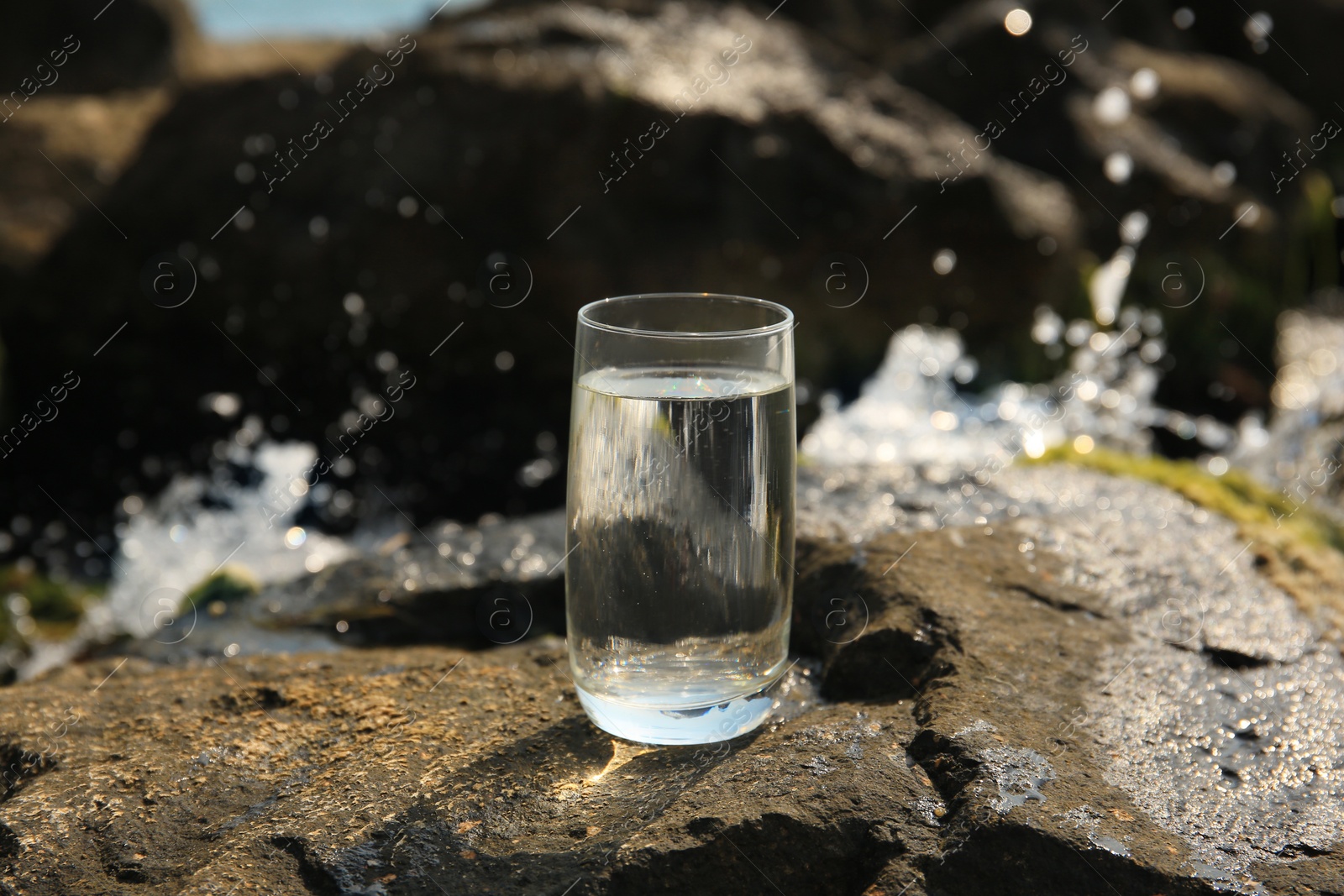 Photo of Glass of fresh water on stone outdoors