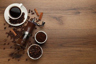 Manual coffee grinder with powder, beans and cup of drink on wooden table, flat lay. Space for text