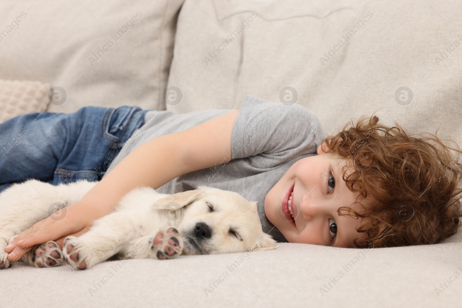 Photo of Little boy hugging cute puppy on couch