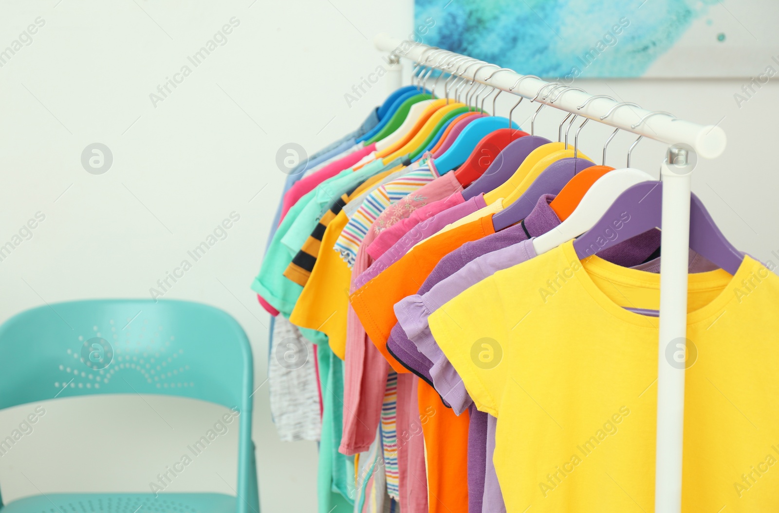 Photo of Different child's clothes hanging on rack indoors. Space for text