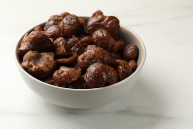 Roasted edible sweet chestnuts in bowl on white marble table, closeup