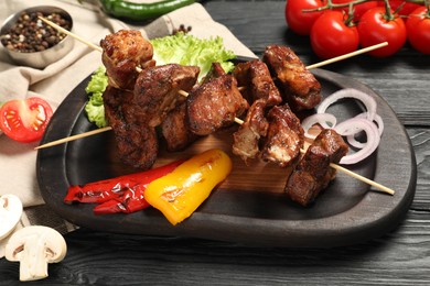 Delicious shish kebabs with vegetables and spices on black wooden table