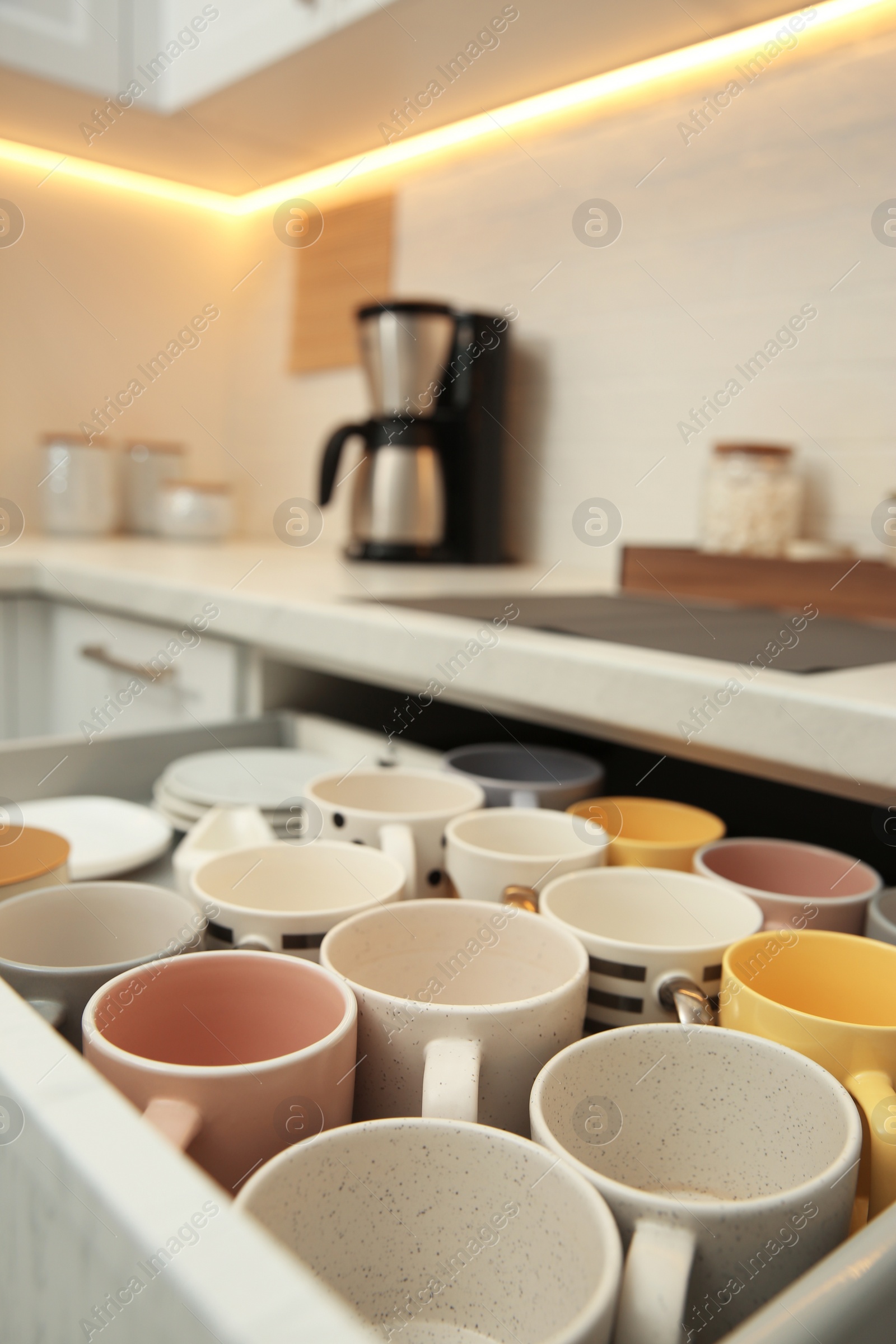 Photo of Open drawer with cups and coffeemaker on countertop in kitchen