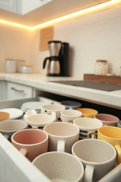 Photo of Open drawer with cups and coffeemaker on countertop in kitchen