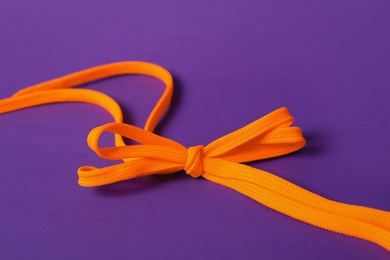 Photo of Orange shoe laces tied in bow on purple background