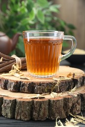 Aromatic licorice tea in cup and dried sticks of licorice root on black wooden table