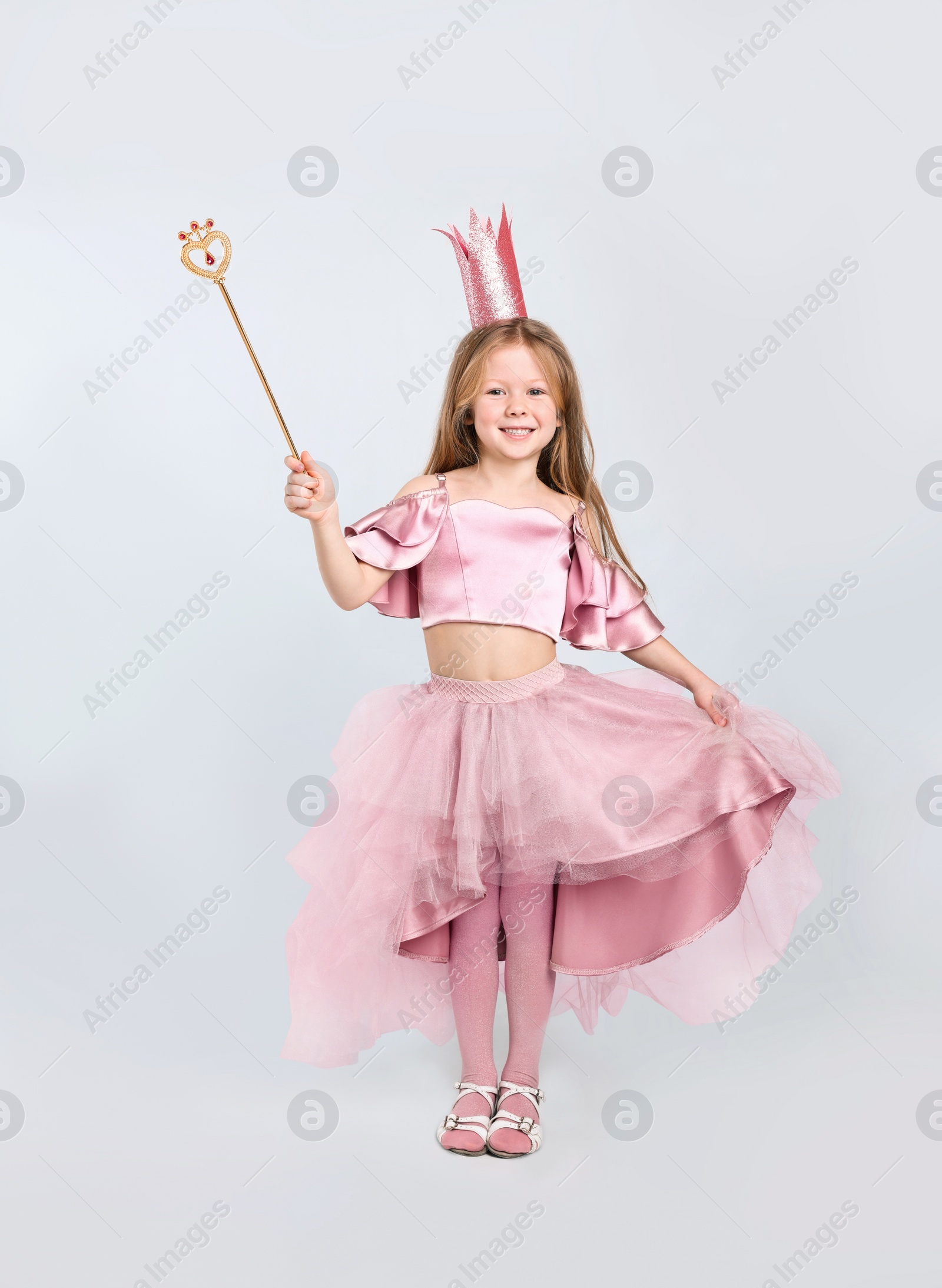 Photo of Cute girl in fairy dress with pink crown and magic wand on light grey background. Little princess