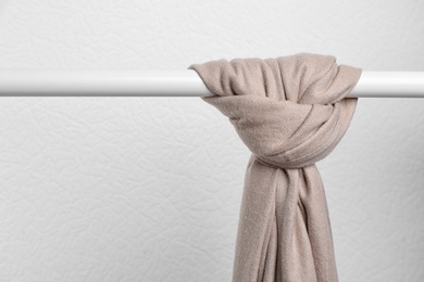 Photo of Brown scarf on wardrobe rack against light background, space for text. Autumn clothes