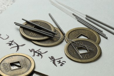 Photo of Acupuncture needles and Chinese coins on paper with characters, closeup