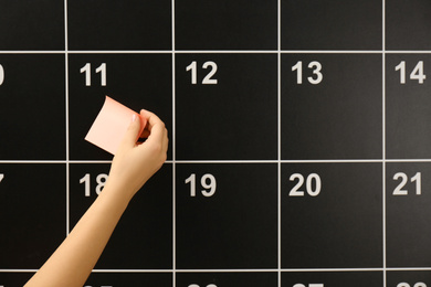 Woman putting sticker on board calendar, closeup