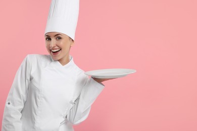 Photo of Happy professional confectioner in uniform holding empty plate on pink background. Space for text