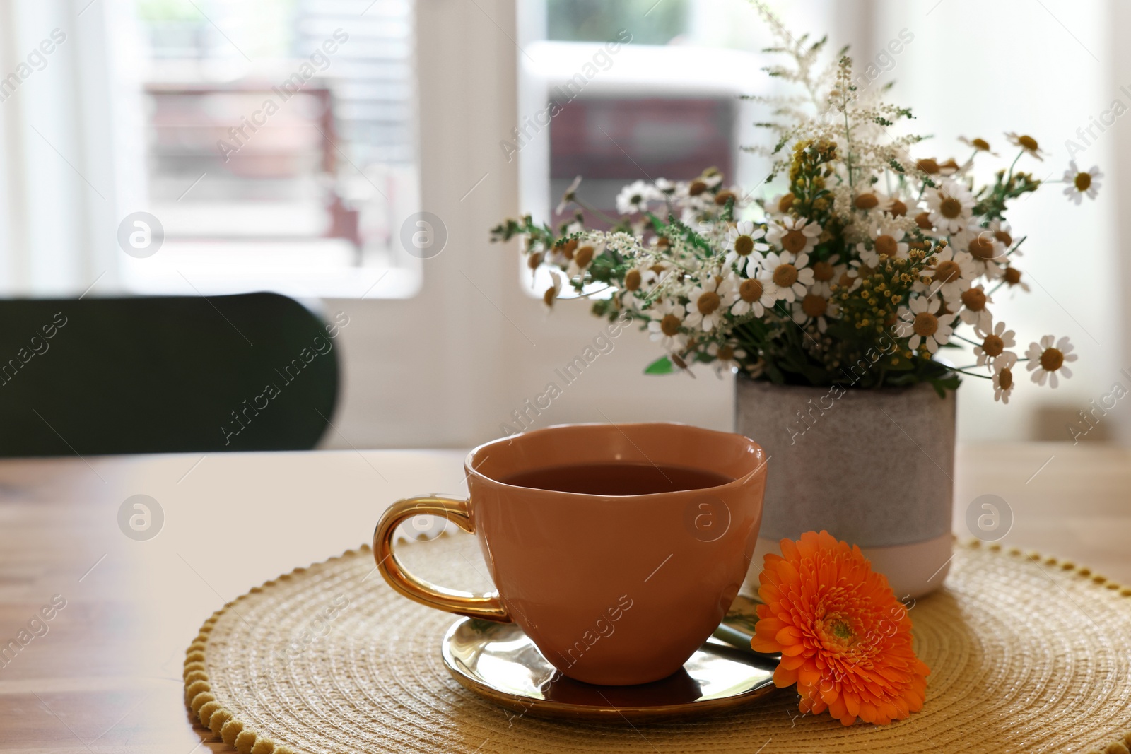 Photo of Cup of delicious chamomile tea and fresh flowers on table in room. Space for text