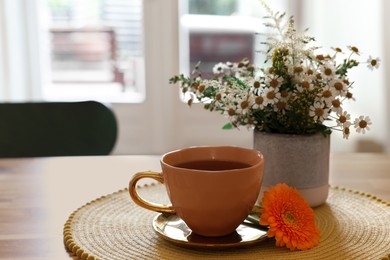 Photo of Cup of delicious chamomile tea and fresh flowers on table in room. Space for text