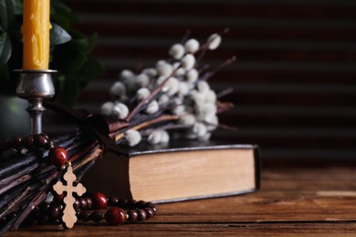Rosary beads, Bible, church candle and willow branches on wooden table, closeup. Space for text