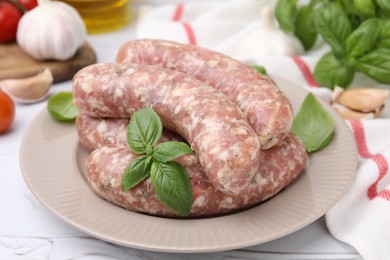 Photo of Raw homemade sausages and basil leaves on white table, closeup