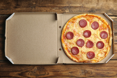 Photo of Tasty pepperoni pizza in cardboard box on wooden table, top view