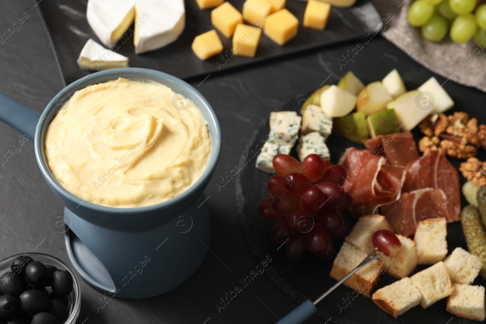 Photo of Fondue with tasty melted cheese, fork and different snacks on black table