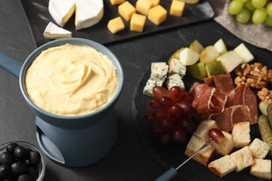 Photo of Fondue with tasty melted cheese, fork and different snacks on black table