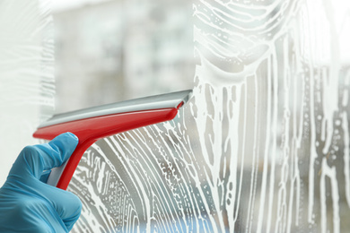 Woman cleaning window with squeegee indoors, closeup