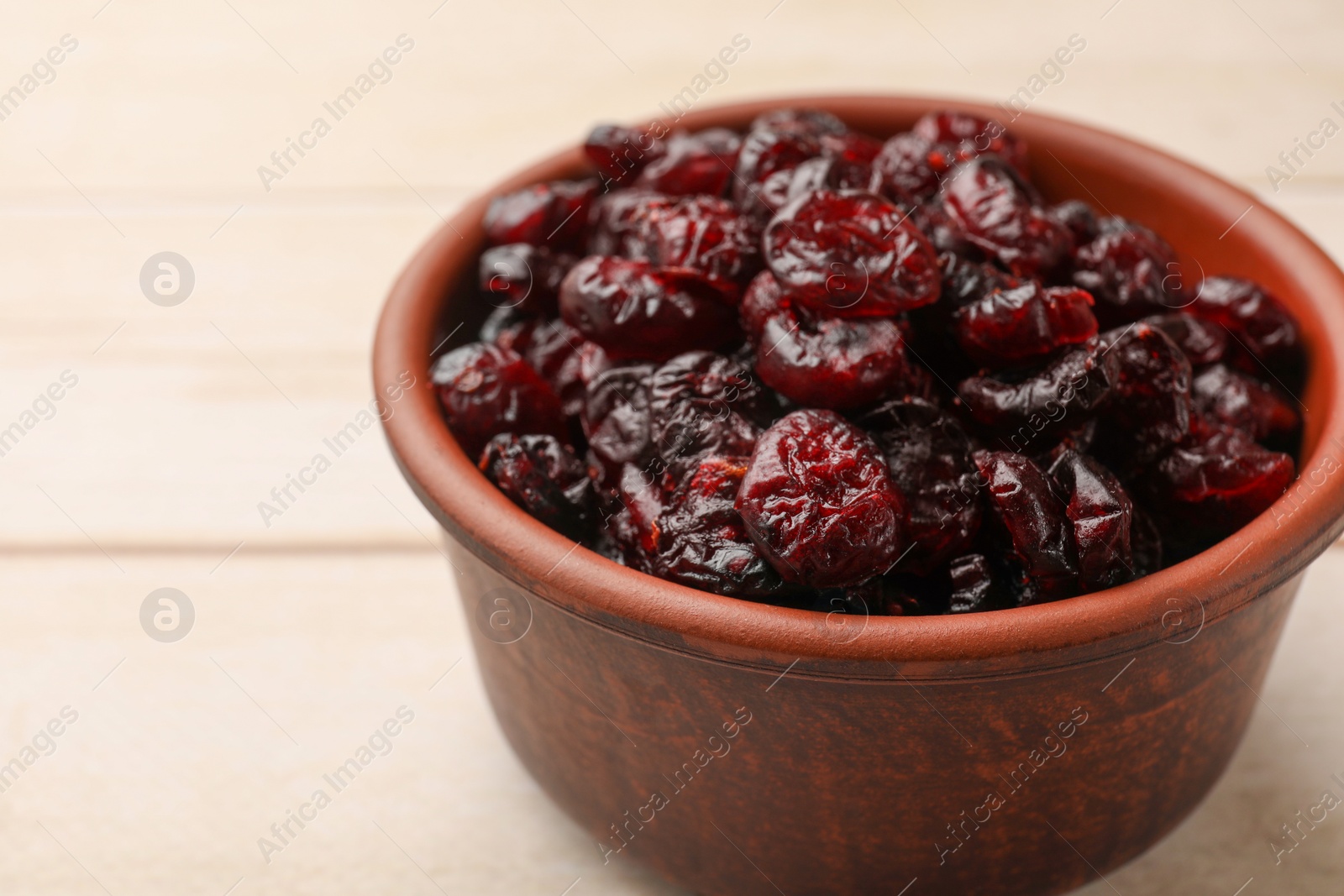 Photo of Tasty dried cranberries in bowl on light wooden table, closeup