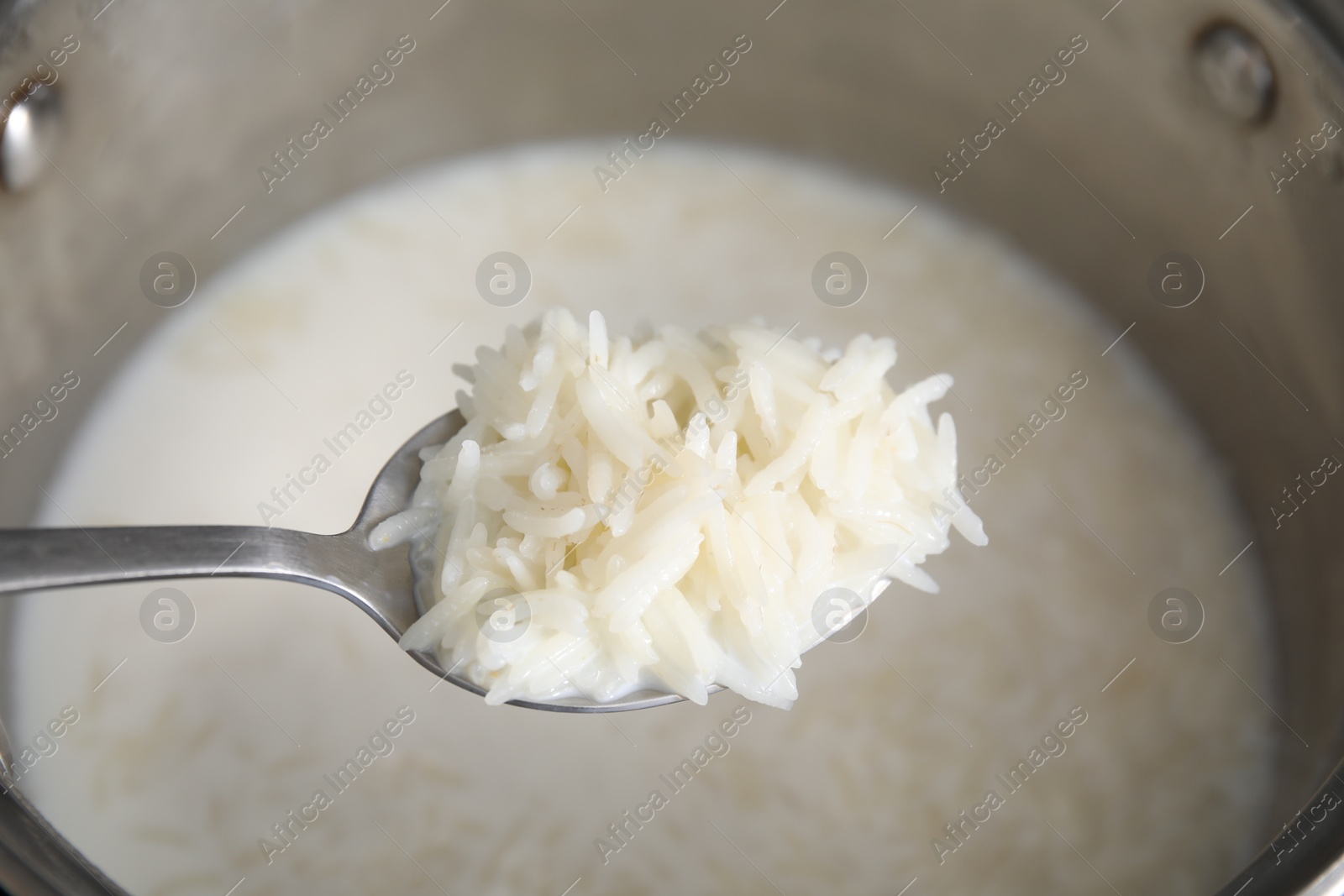 Photo of Spoon with tasty rice porridge over pot, closeup