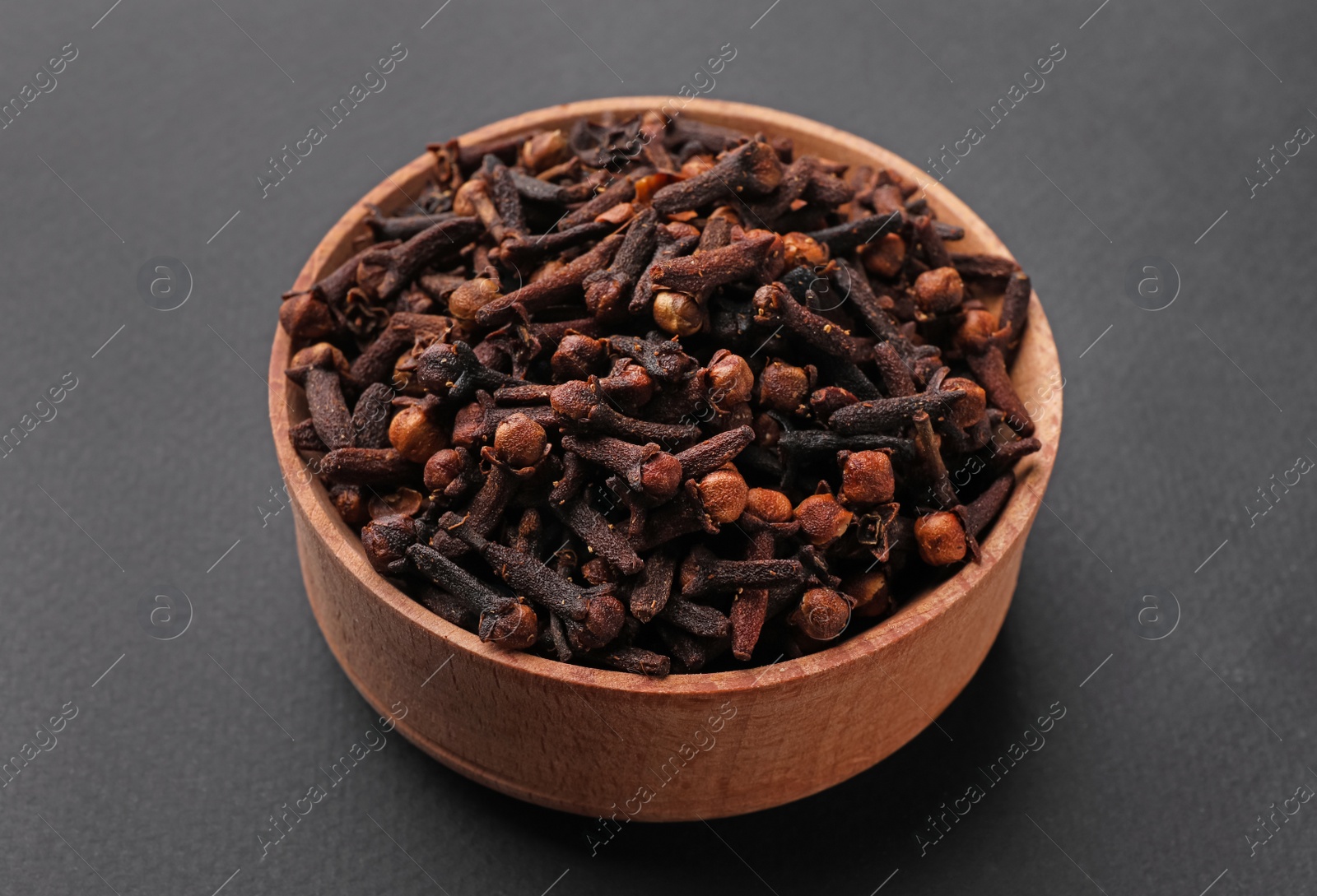 Photo of Aromatic dry cloves in wooden bowl on grey background, closeup