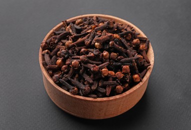 Photo of Aromatic dry cloves in wooden bowl on grey background, closeup