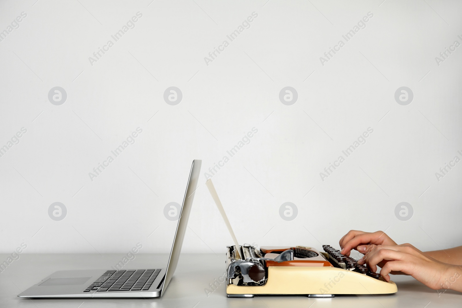 Photo of Woman using old typewriter near laptop at table against light background, closeup with space for text. Concept of technology progress